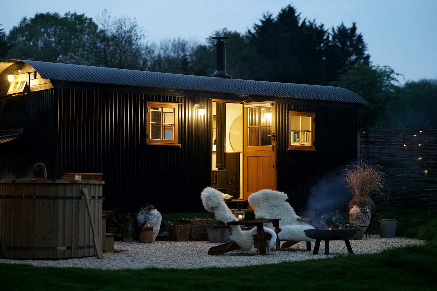 Hazel, a black-clad hut glowing at dusk with a wood-fired hot tub and firepit